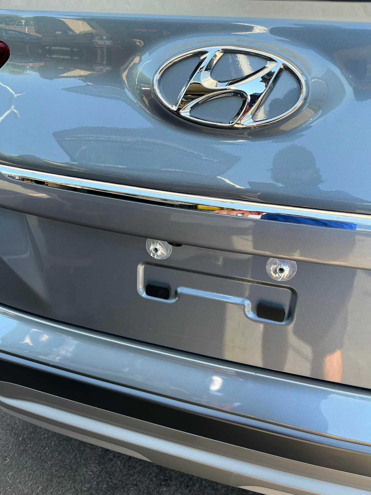 A chrome Hyundai emblem centered above a rectangular license plate mounting area on a gray car trunk.