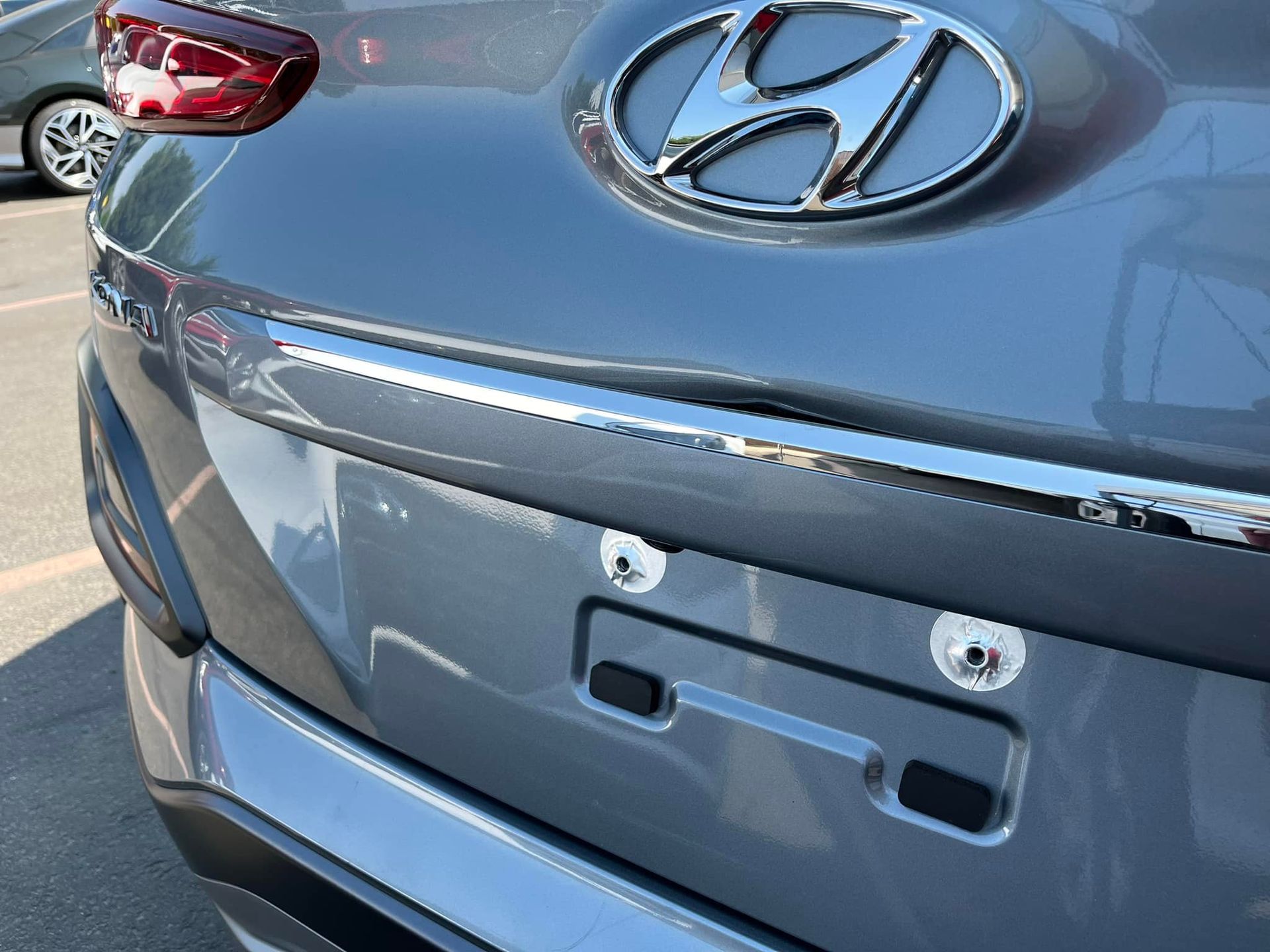 Rear view of a grey Hyundai SUV showing the brand logo, chrome trim above the license plate area, and two bolt holes.