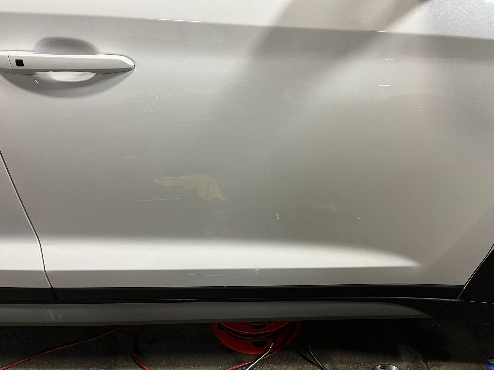 Close-up of a white car door showing surface scratches and paint scuffs near the black lower trim.