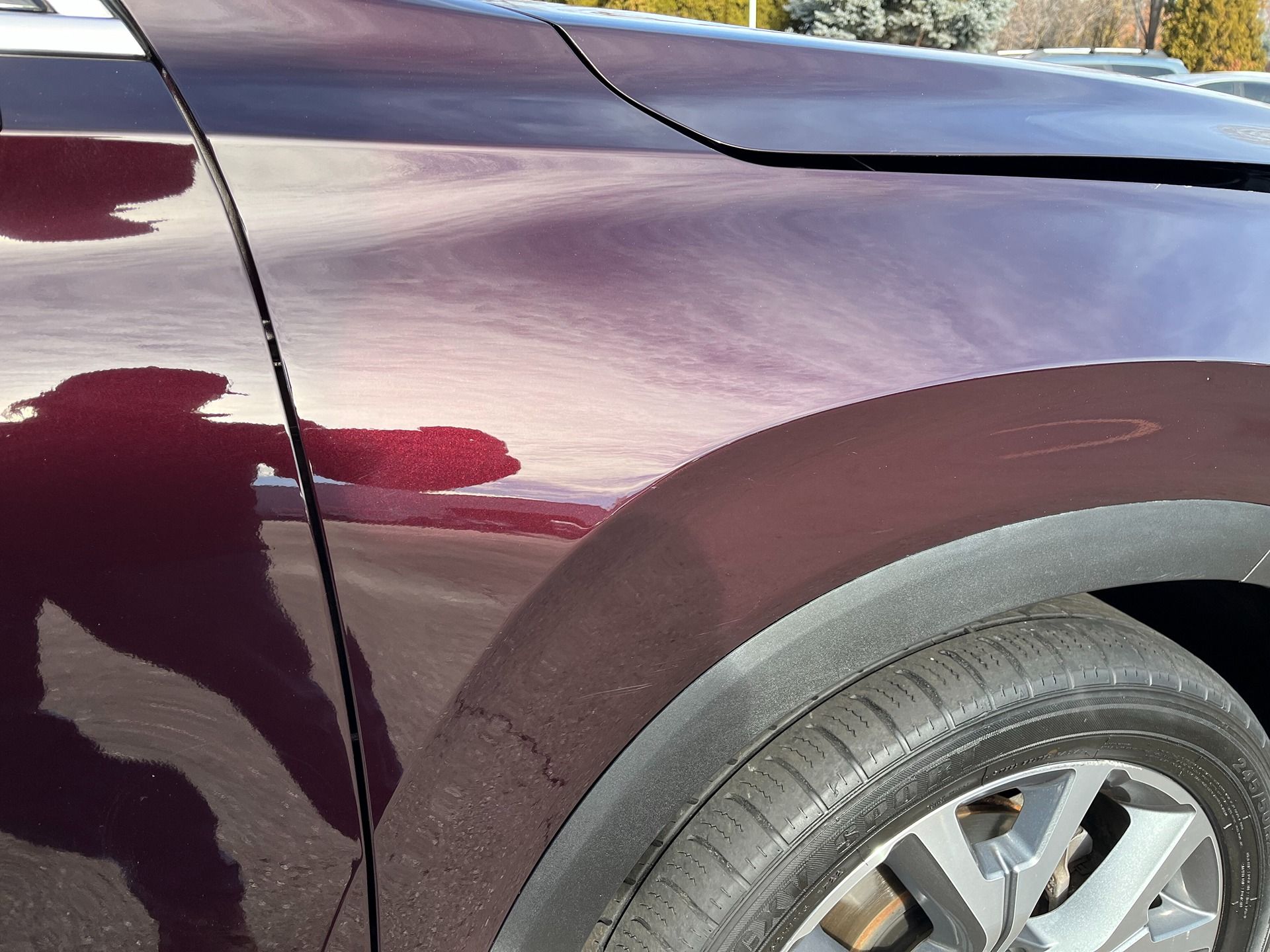 A close-up view of a dark maroon car's front fender and wheel well with a visible body panel misalignment.