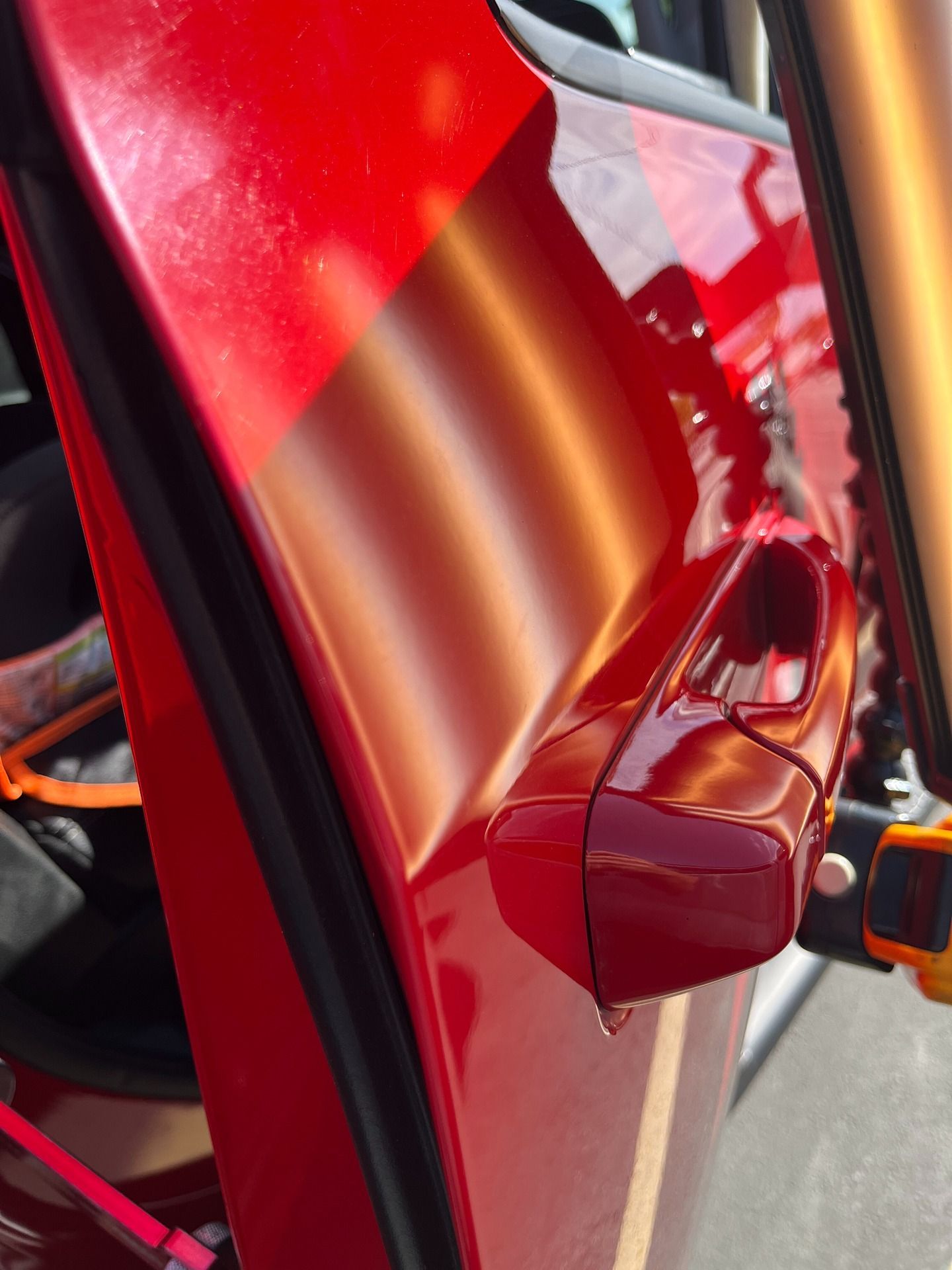 A close-up view of a red car door, showing a prominent dent near the door handle illuminated by a repair light reflection.