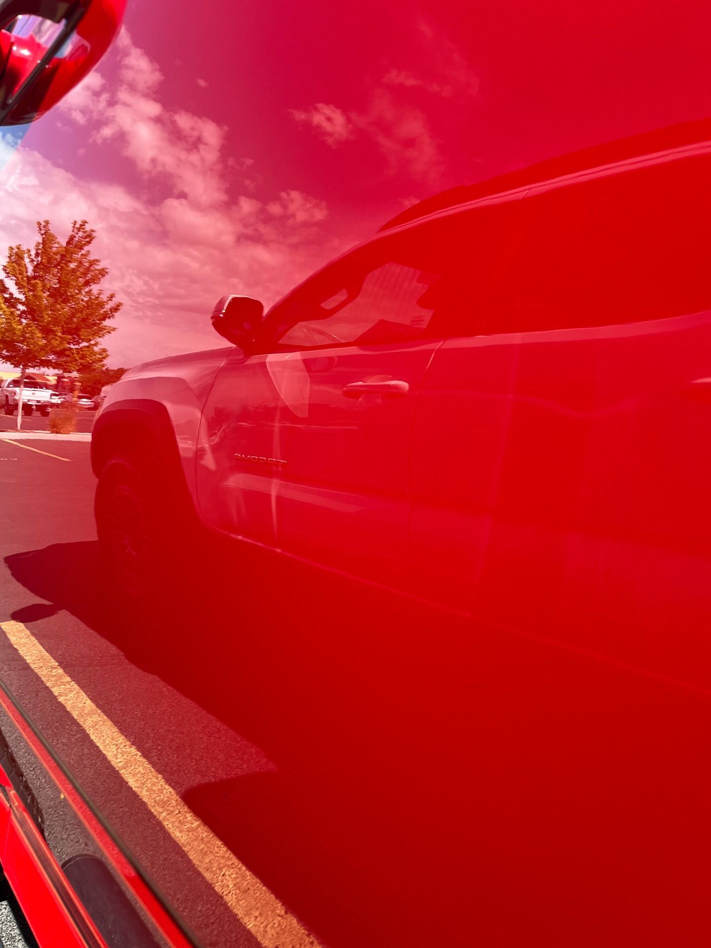A red truck parked in a lot, with the sky and clouds reflected in its side panel.