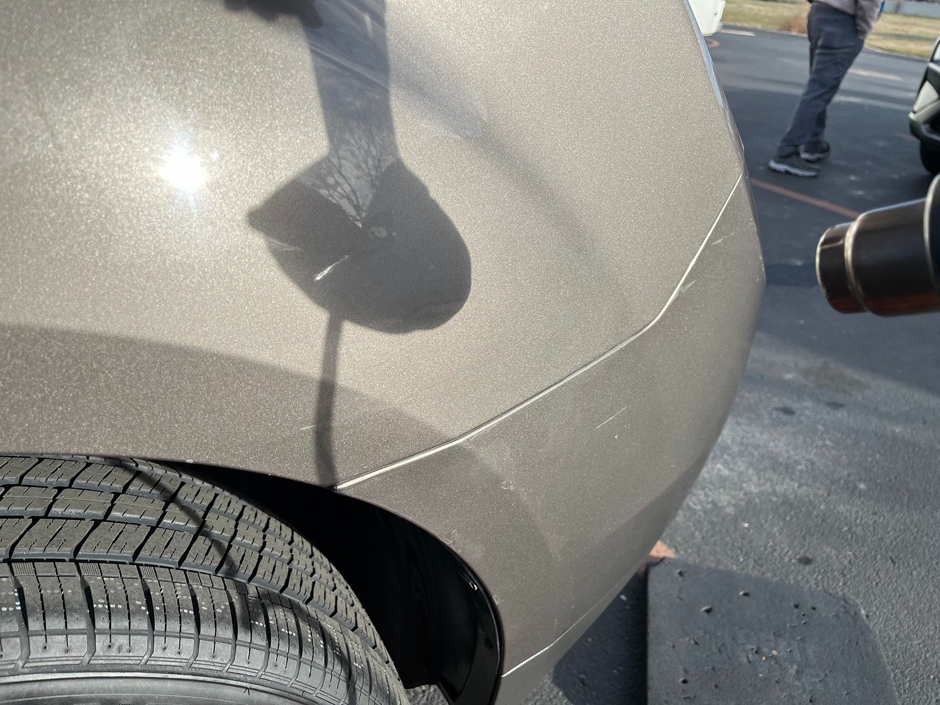 A person uses a heat gun to repair a dent on the rear panel of a metallic brown vehicle.