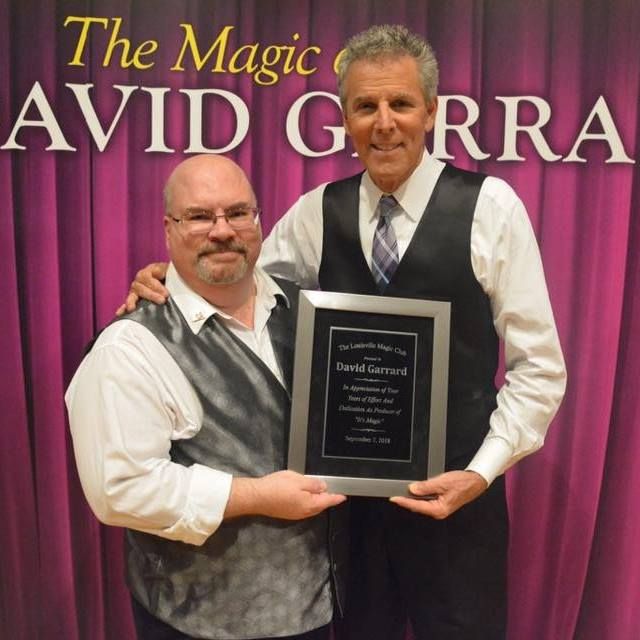 Man in black shirt holding a certificate presenting to another gentleman in white shirt and black vest