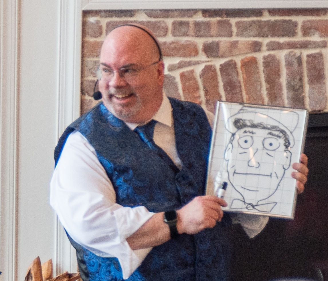 A person in a blue vest and white shirt holds a framed cartoon sketch of a man wearing a hat and bow tie.