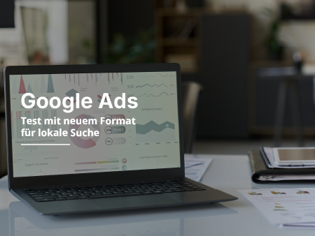 Auf einem Tisch steht ein Laptop mit einem Google-Ads-Dashboard. Daneben liegen verschiedene Notizbl