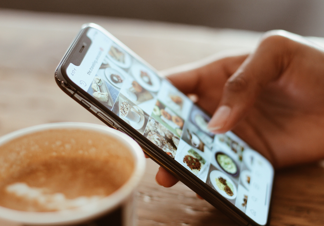 Eine Person hält ein Mobiltelefon neben einer Tasse Kaffee.