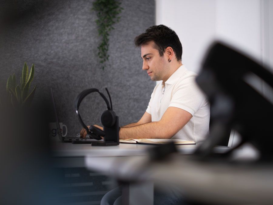 Ein Mann sitzt mit einem Laptop und Kopfhörern an einem Schreibtisch.