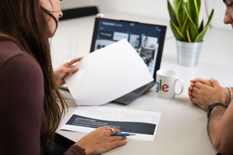 Eine Frau hält ein Blatt Papier vor einem Laptop.