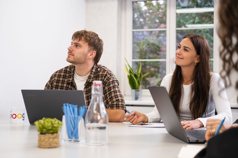 Eine Gruppe von Leuten sitzt um einen Tisch herum und schaut auf einen Laptop.