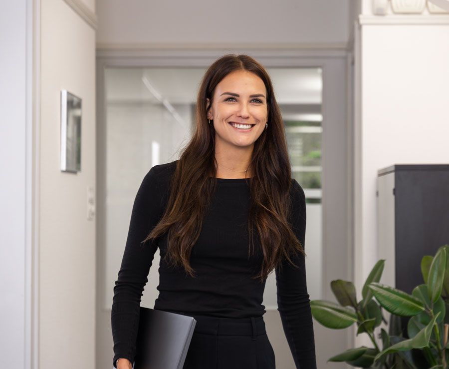 Eine Frau in einem schwarzen Kleid hält einen Laptop und lächelt.