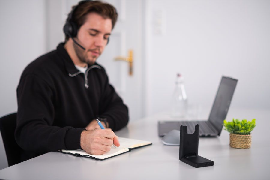 Ein Mann mit Kopfhörern sitzt an einem Schreibtisch und schreibt in ein Notizbuch.