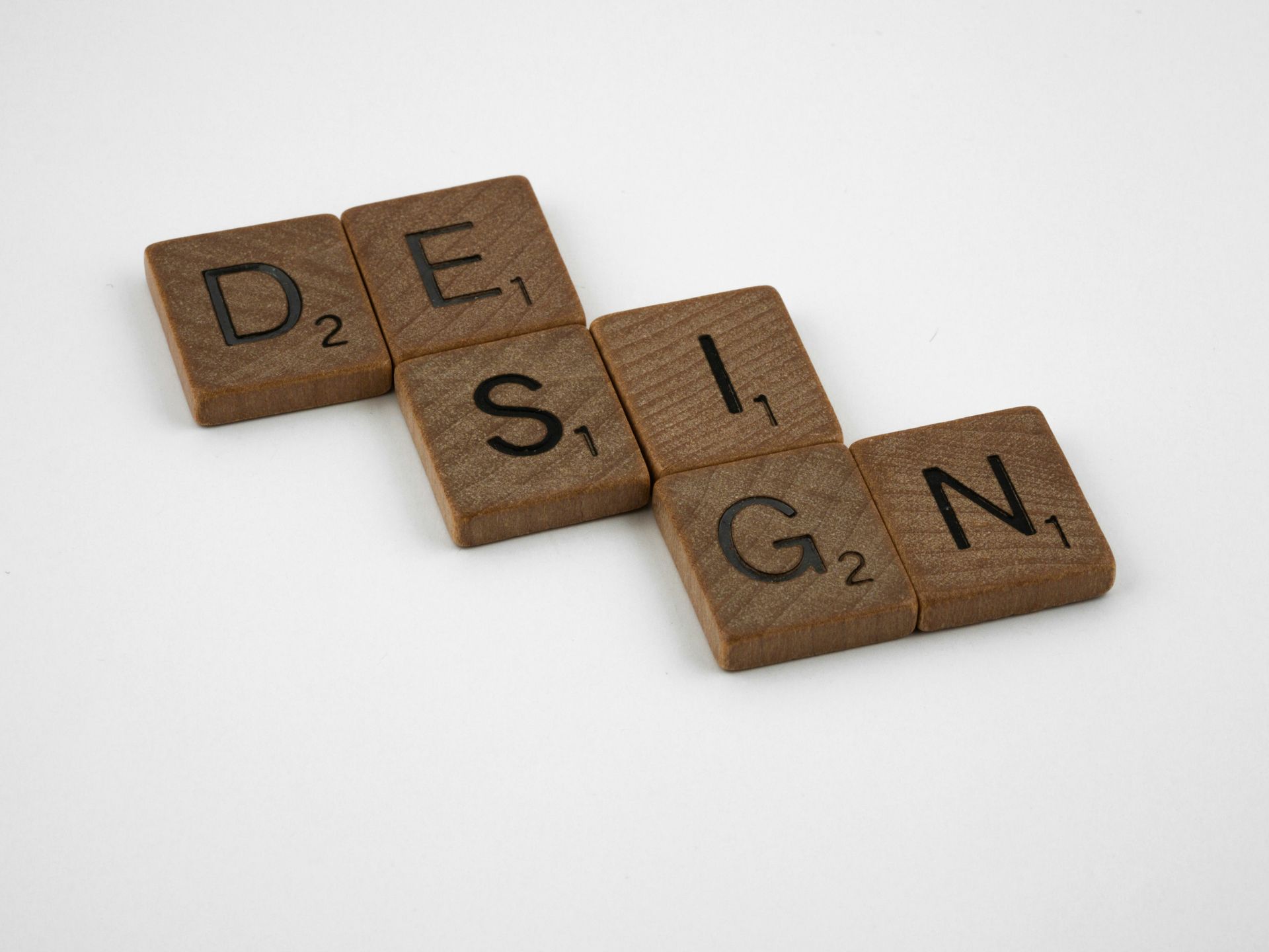 „DESIGN“ in braunen Scrabble-Steinen auf weißem Hintergrund.