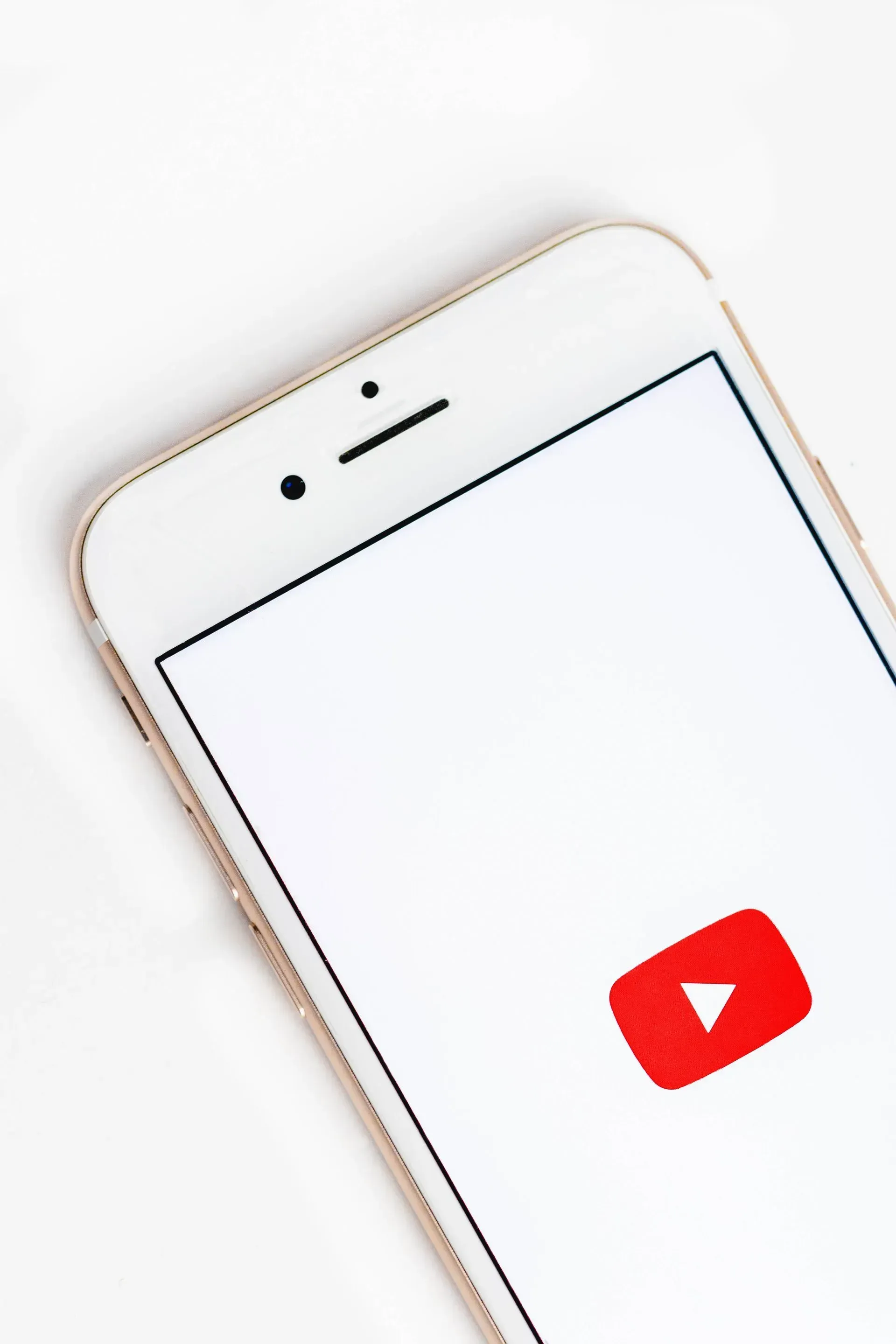 Ein weißes Smartphone mit dem YouTube-Logo auf einem weißen Bildschirm. Das Telefon ist schräg vor einem weißen Hintergrund positioniert.