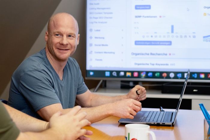 Zwei Männer stehen an einem Tisch und schauen auf einen Laptop.