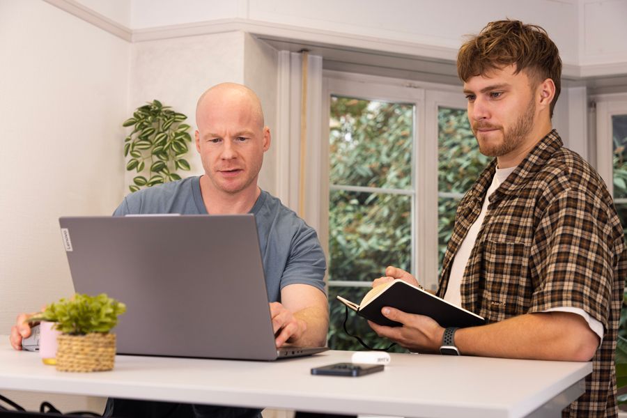 Zwei Männer sitzen an einem Tisch und schauen auf einen Laptop.