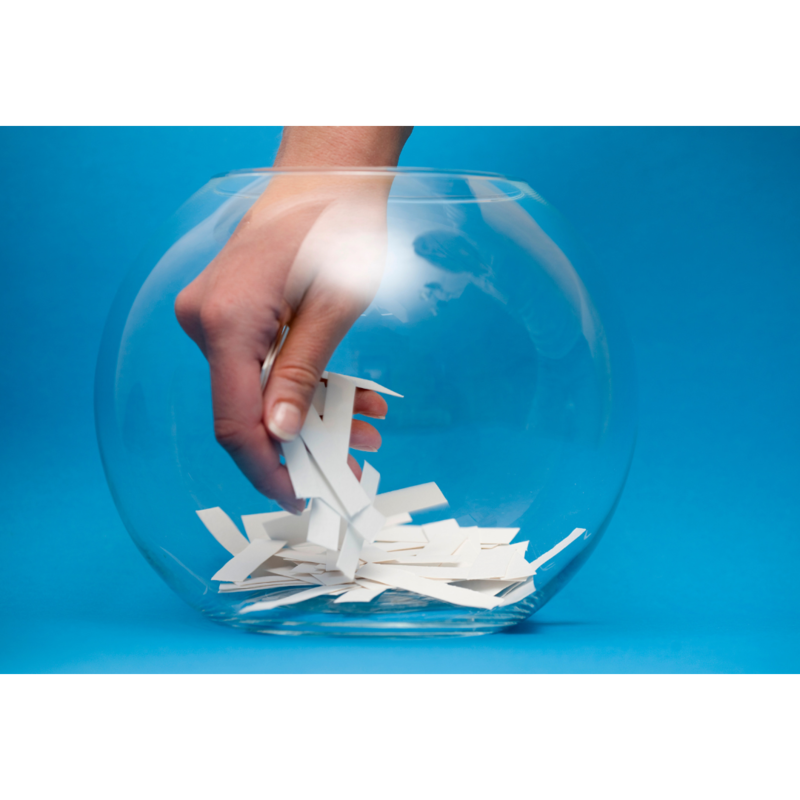 A hand is reaching into a glass bowl filled with pieces of paper