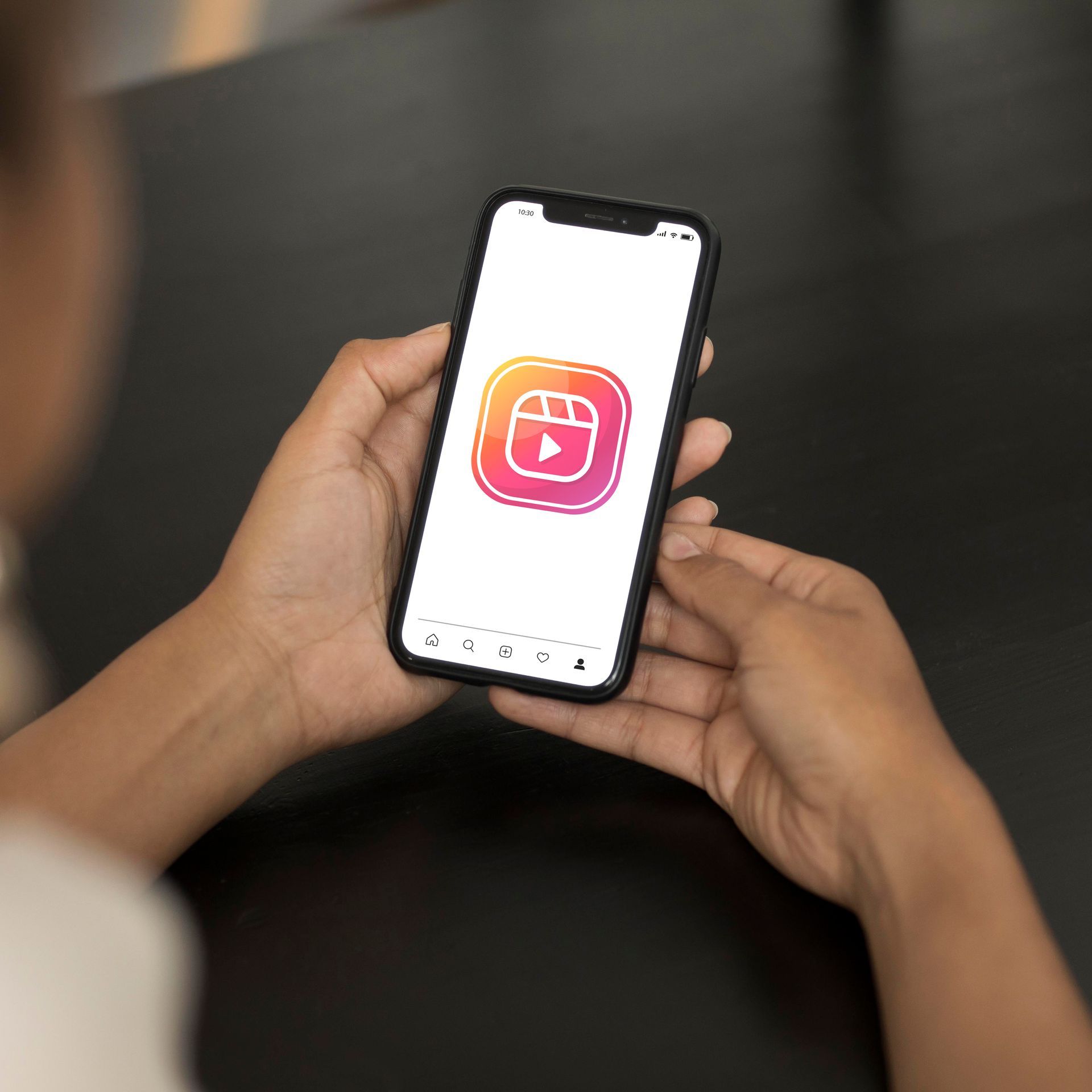 Hände halten ein Smartphone, auf dessen weißem Bildschirm das Instagram Reels-Logo angezeigt wird.