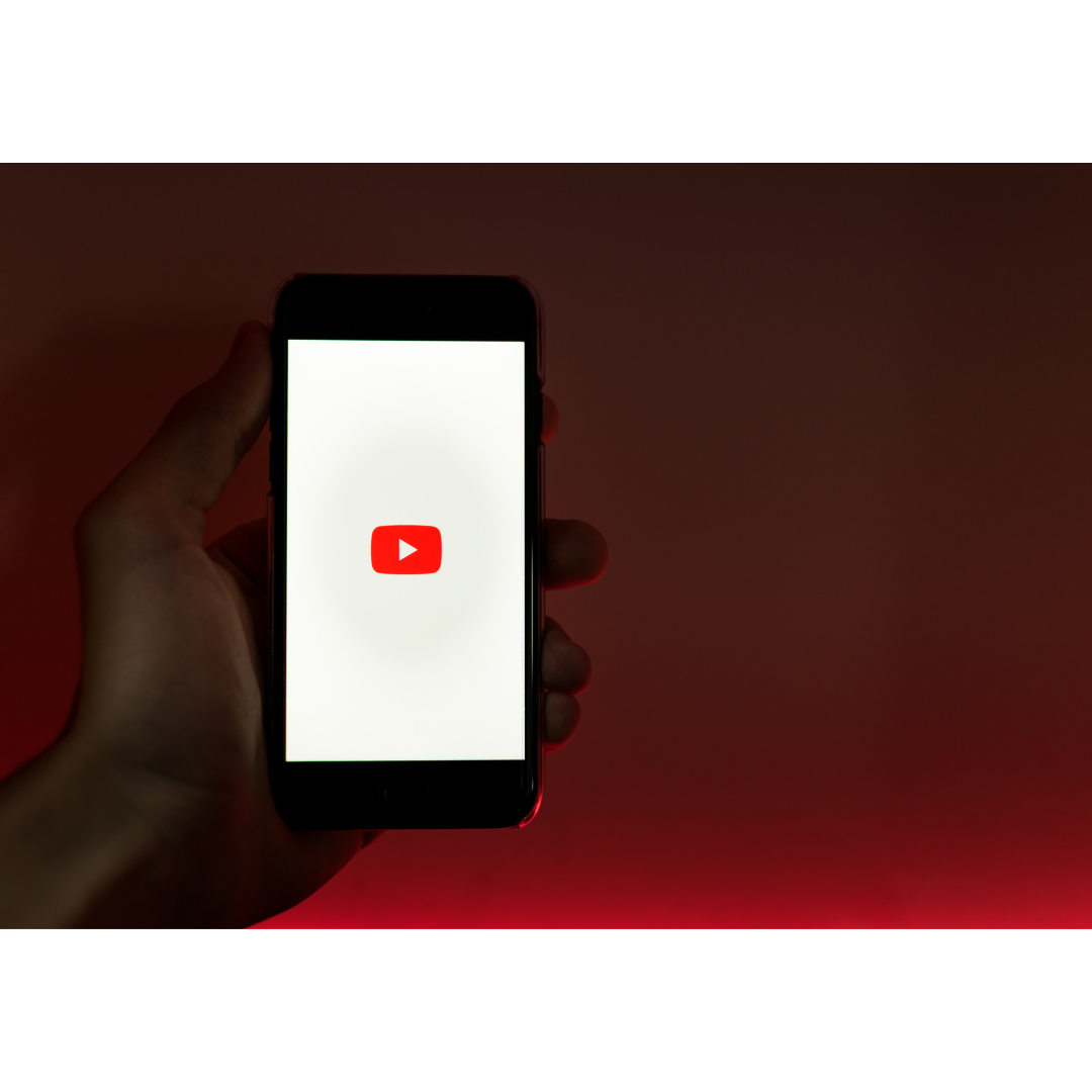 Eine Person hält ein Handy in der Hand, auf dessen Bildschirm ein Youtube-Logo zu sehen ist.