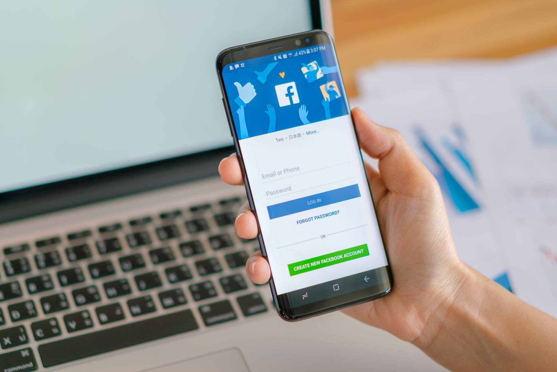 A person is holding a cell phone in front of a laptop.