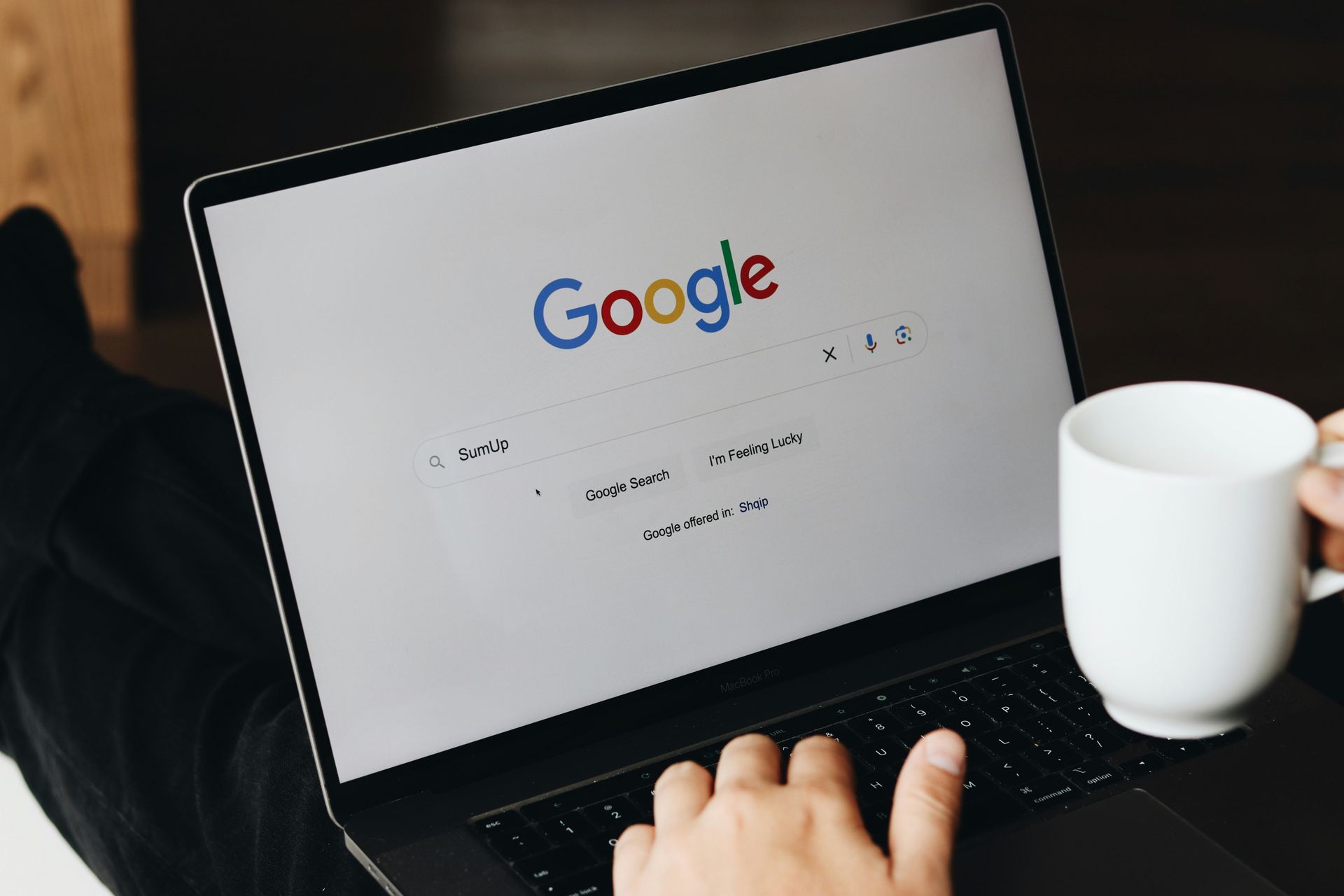 Eine Person tippt auf einem Laptop-Computer, während sie eine Tasse Kaffee in der Hand hält.