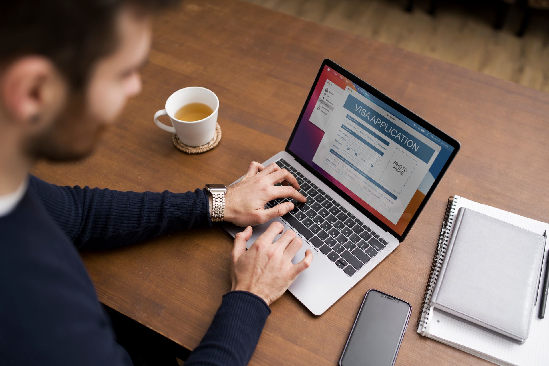 Eine Person tippt auf einem Laptop, daneben stehen eine Tasse und mehrere Notizbücher.