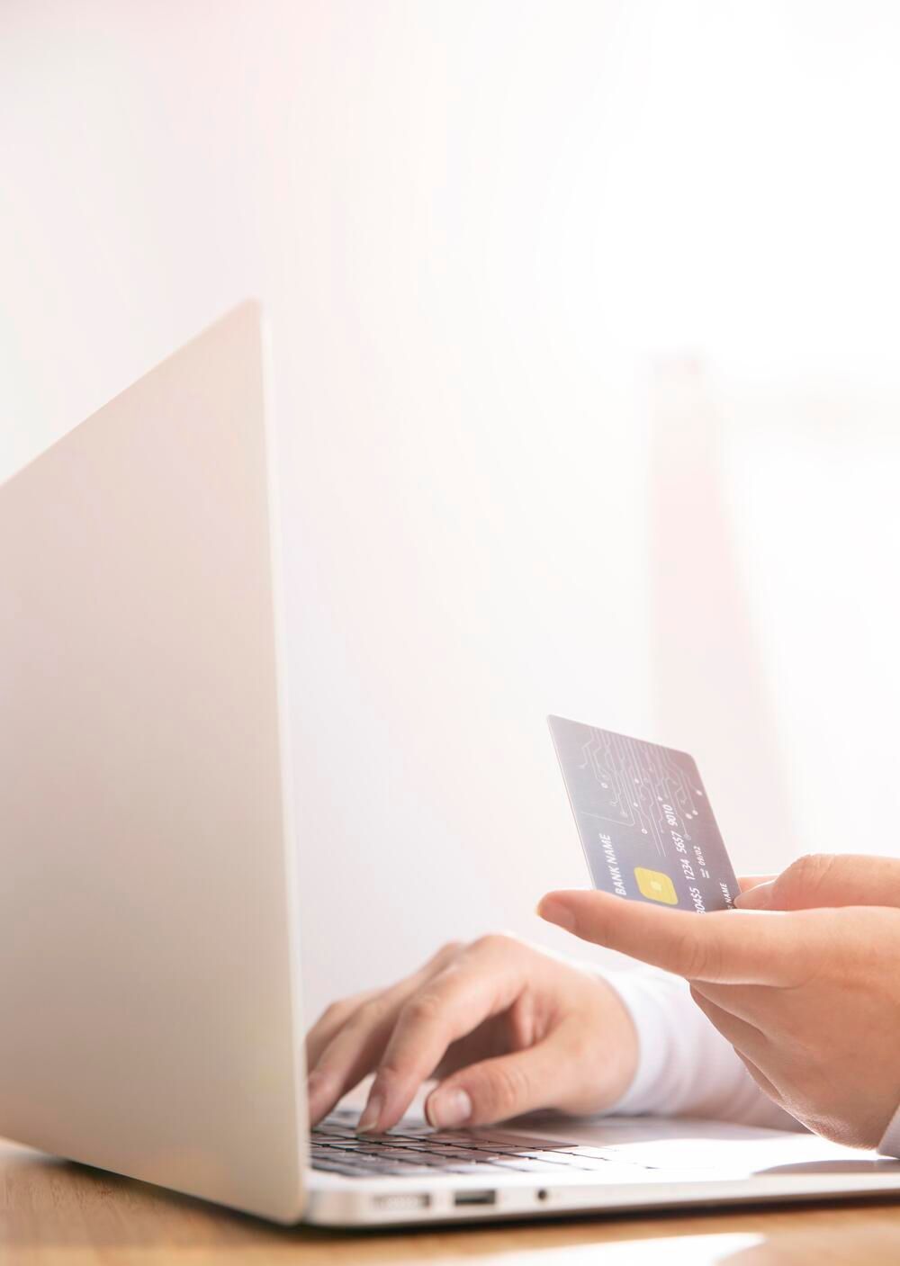 Eine Person hält eine Kreditkarte in der Hand, während sie einen Laptop-Computer benutzt.
