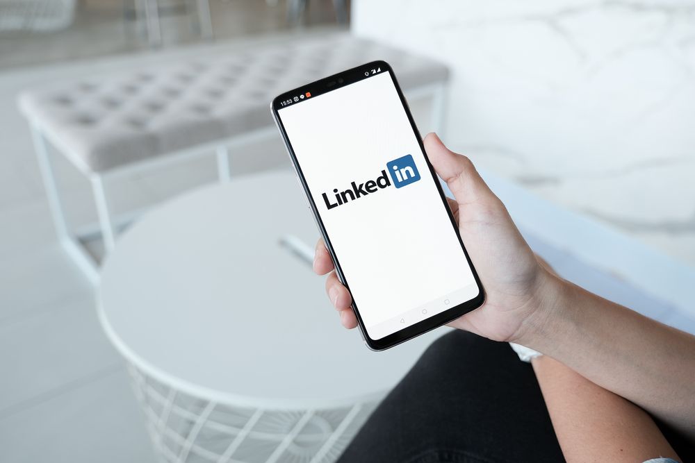 Eine Person hält ein Handy in der Hand, auf dessen Bildschirm Linkedin angezeigt wird.