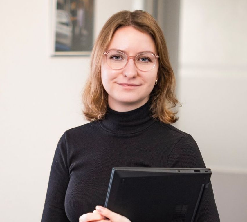 Eine Frau mit lockigem Haar trägt ein weißes Hemd und lächelt.