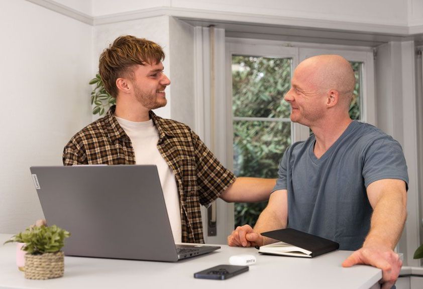 Eine Gruppe von Leuten sitzt um einen Tisch herum und schaut auf einen Laptop.