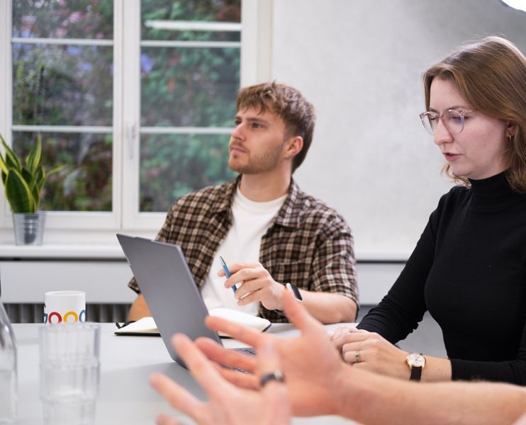 Eine Frau sitzt an einem Tisch und benutzt einen Laptop in einem Meeting.