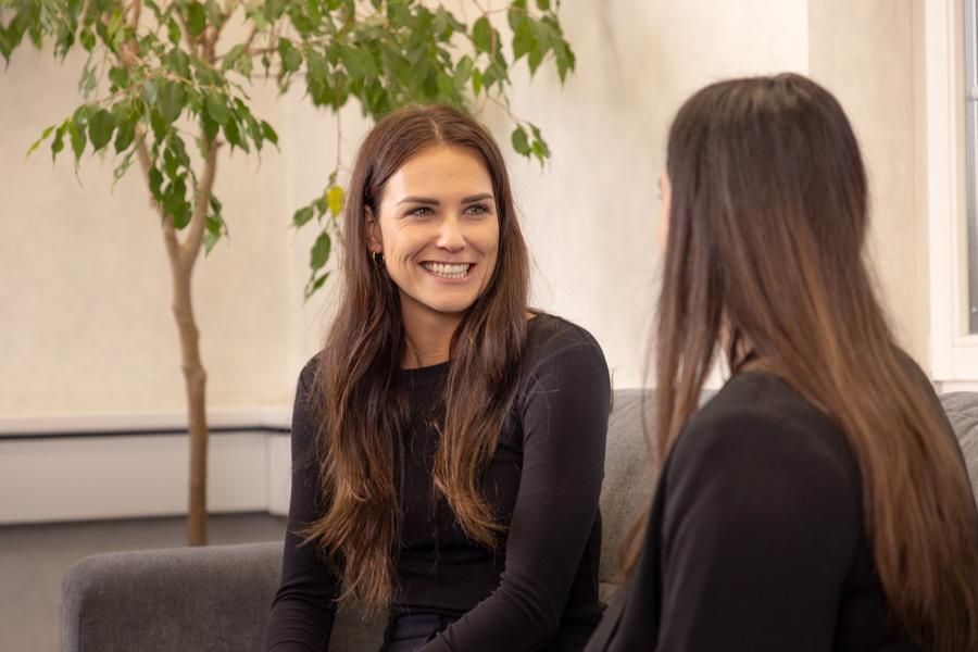 Zwei Frauen sitzen auf grauem Sofa und besprechen etwas.