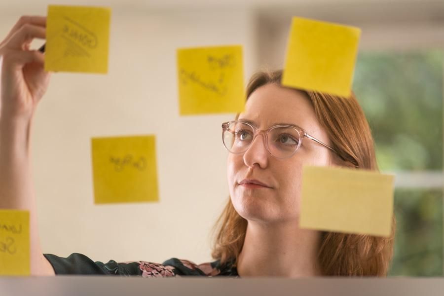 Eine Frau steht hinter einer Glasscheibe und schreibt auf gelbe Post-Its