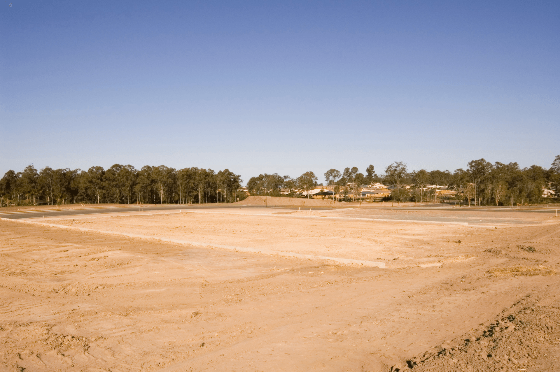 An empty field with trees in the background and a blue sky