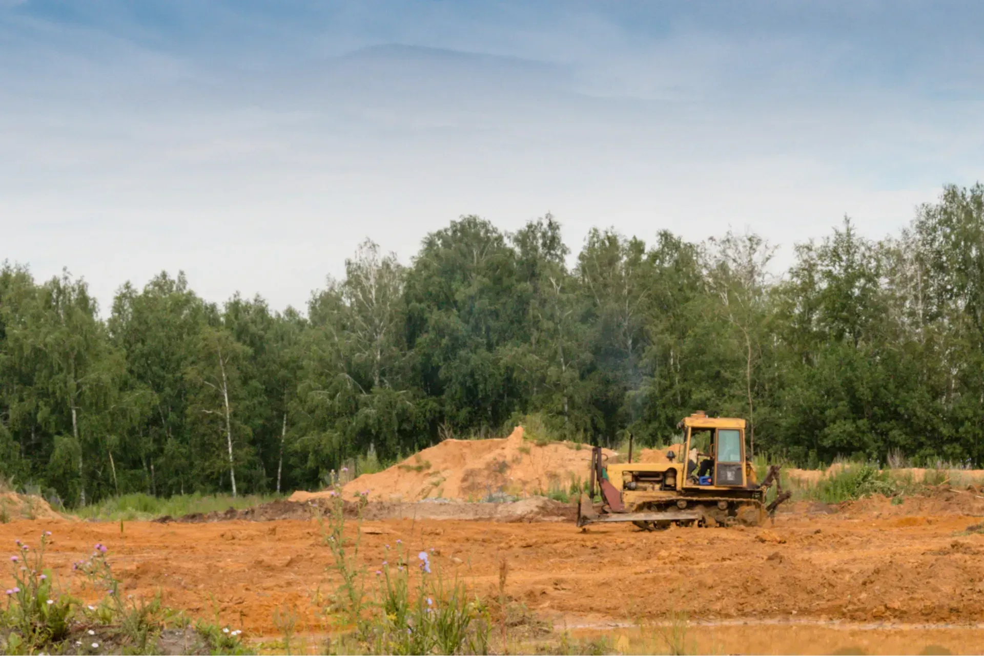 A bulldozer is moving dirt in a field with trees in the background.