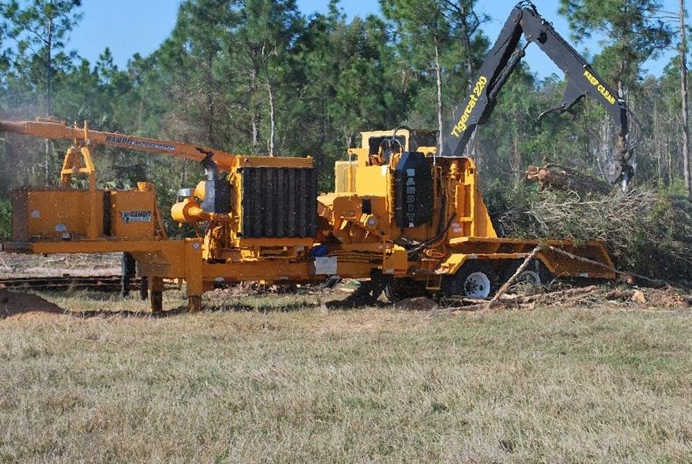 A large yellow machine with a crane attached to it is in a field with trees in the background