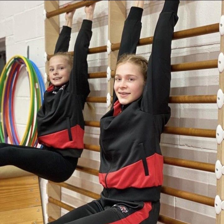 Two girls are doing exercises on a wall with a hula hoop in the background