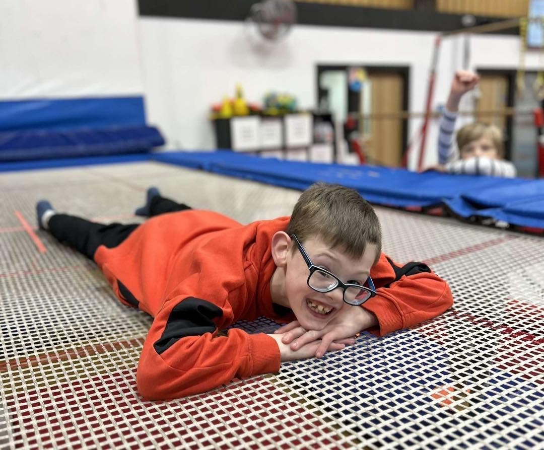 A young boy wearing glasses is laying on a trampoline.