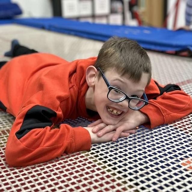 A young boy wearing glasses is laying on a trampoline.