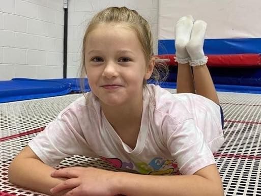 A young girl is laying on her stomach on a trampoline.