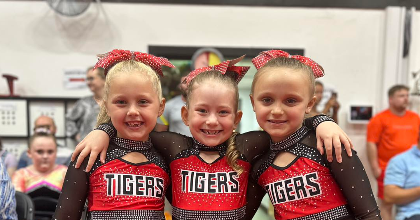 Three cheerleaders are posing for a picture together in a gym.