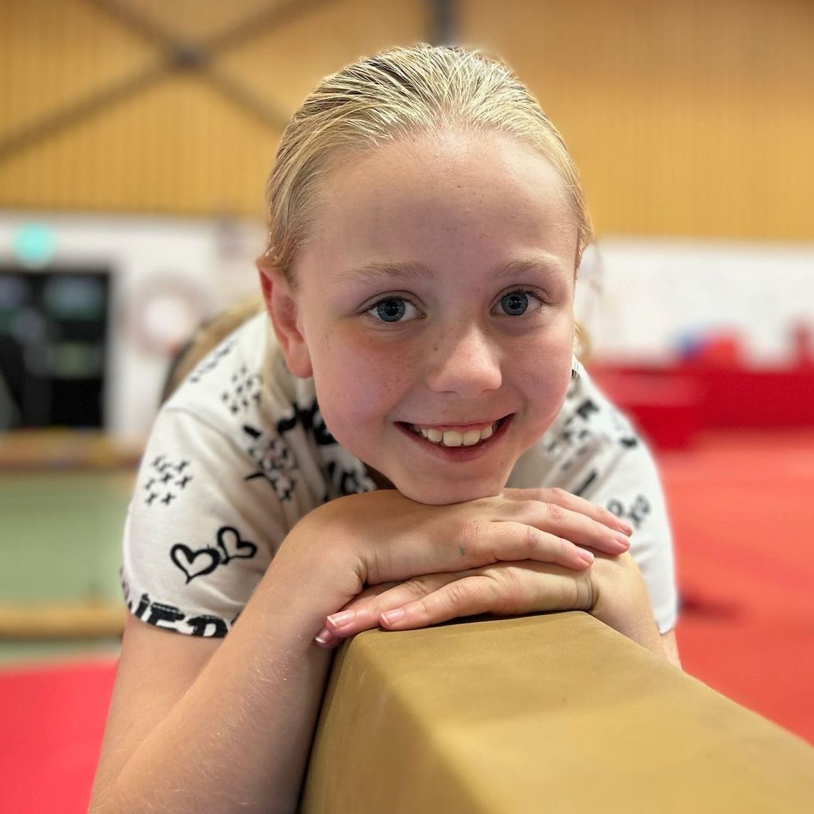 A young girl is leaning on a balance beam and smiling