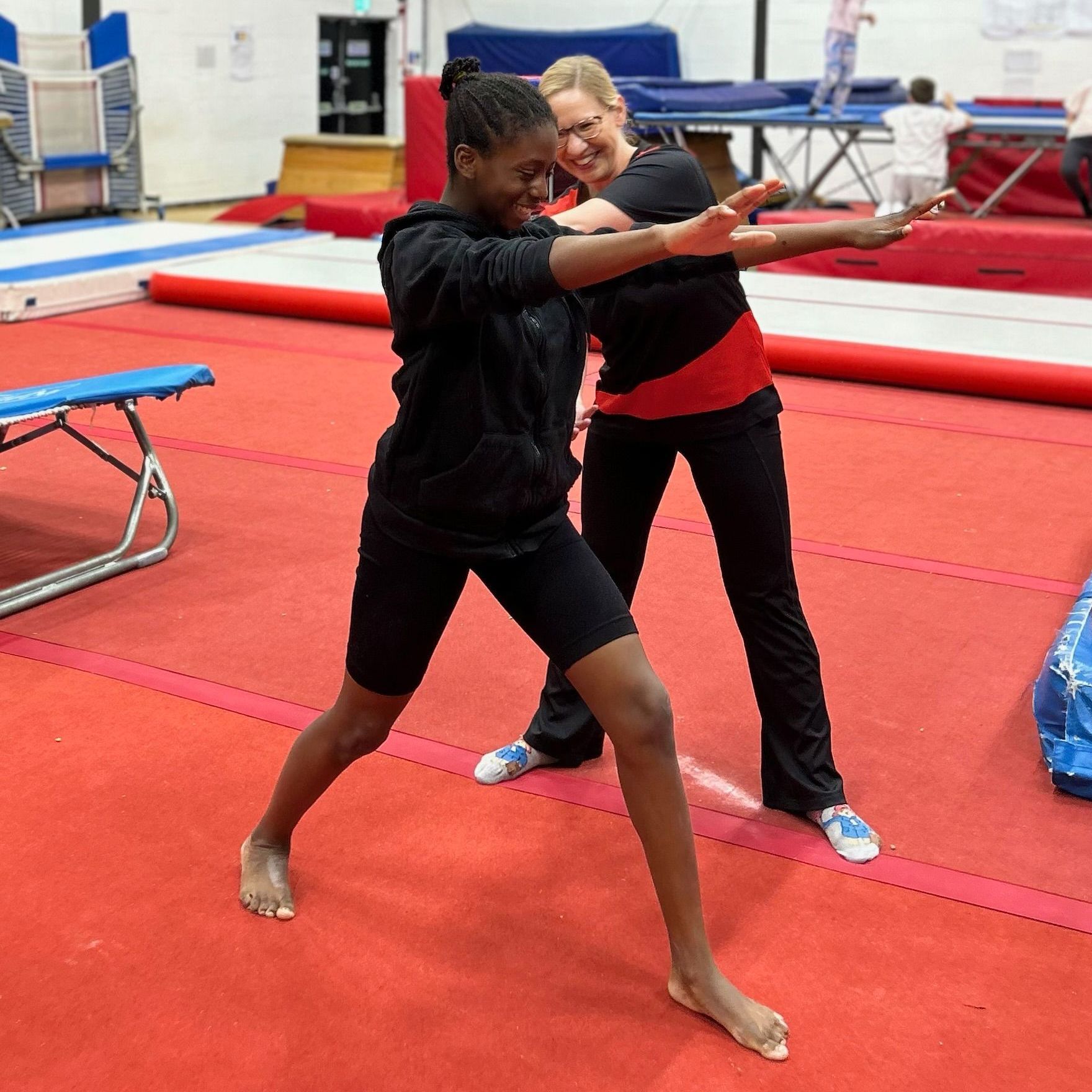 Two women are standing next to each other on a red mat in a gym.