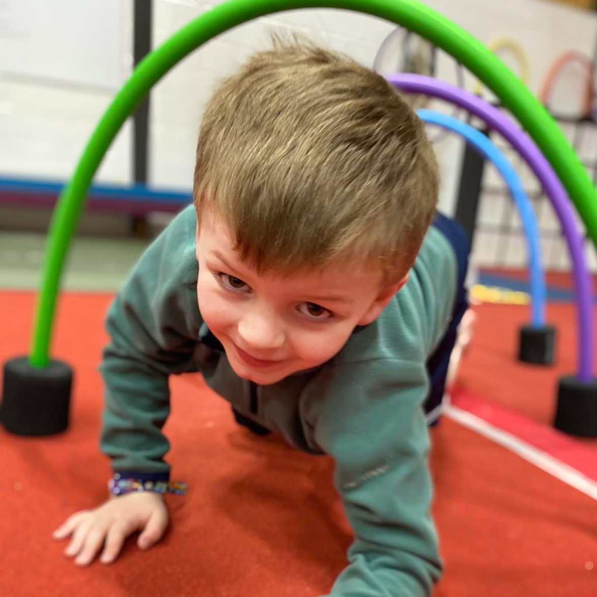 A young boy is crawling under a green and purple arch.