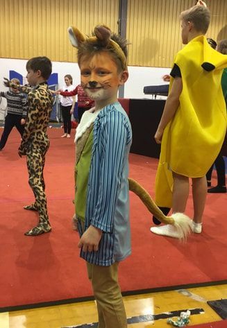 A boy in a lion costume is standing on a gym floor.