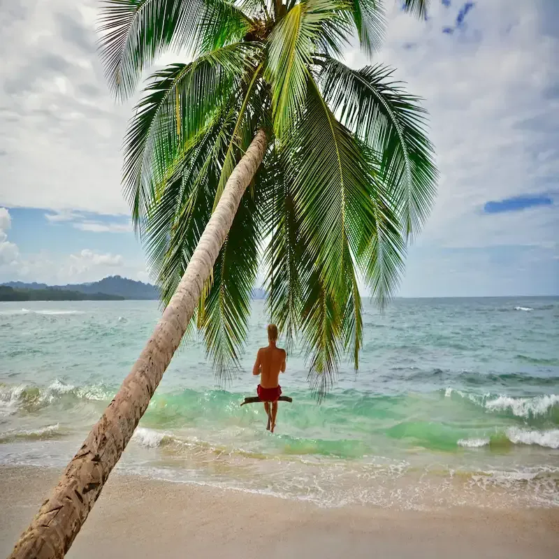 Child running toward a leaning palm tree on the shore of Playa Limón, with the Caribbean Sea in the background in Miches, Dominican Republic
