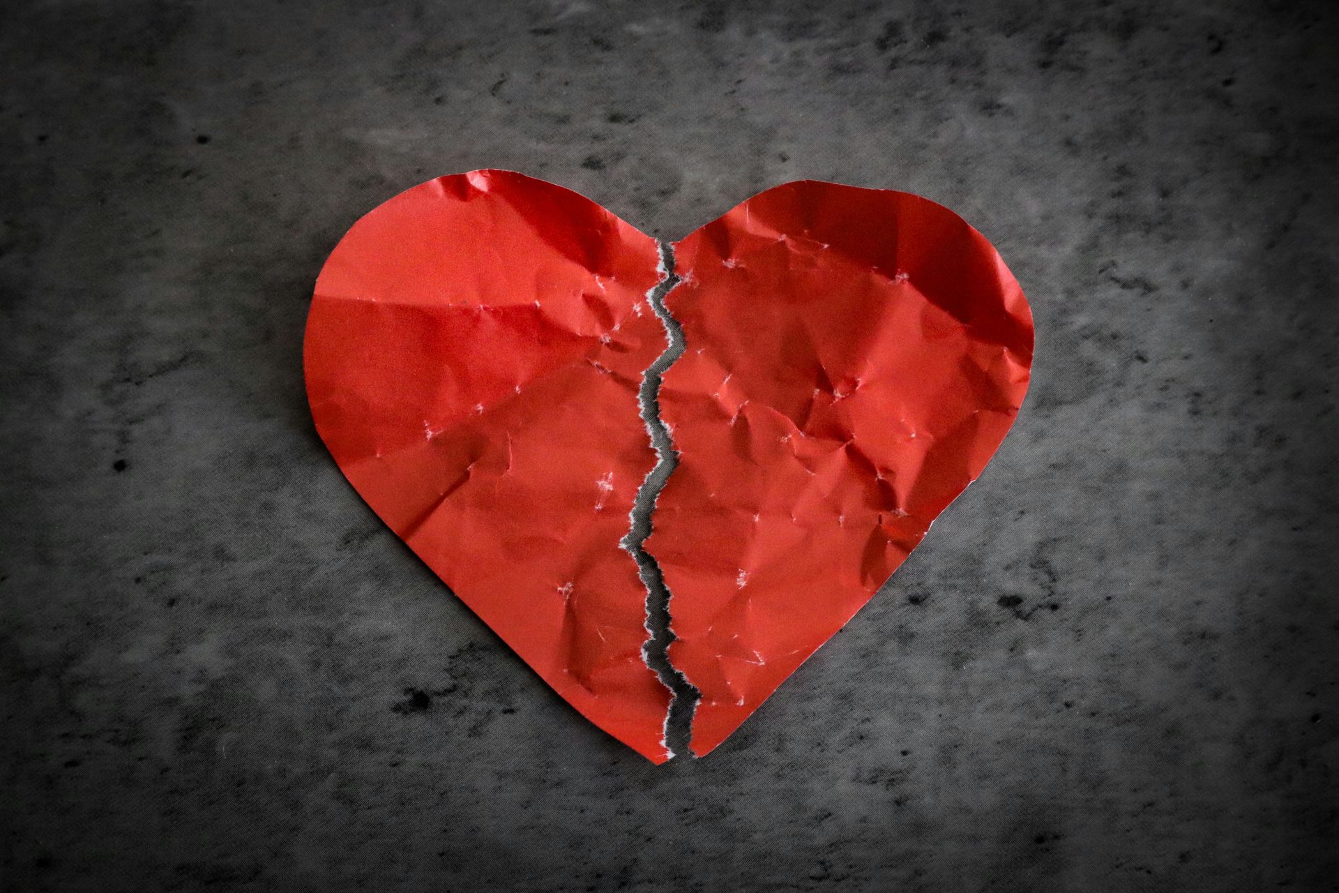 A broken red heart is sitting on a gray surface