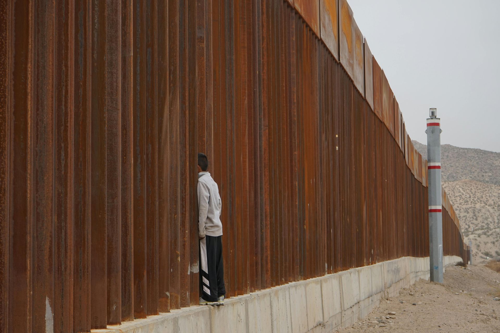 A man is leaning against a rusty fence