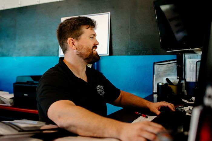 A man with a beard is smiling while sitting in front of a computer.