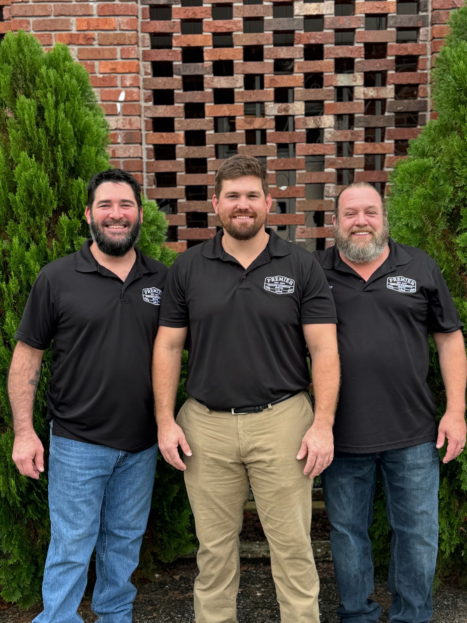 Three men are posing for a picture in front of a brick wall.